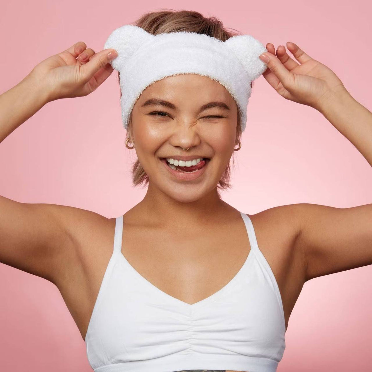 Smiling woman wearing fluffy white headband with bear ears against pink background